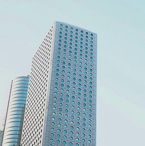Tall office building with a blue glass facade and round window patterns, against a light sky background.