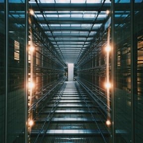 A view inside a data center server room with tall server racks on both sides and a central aisle.