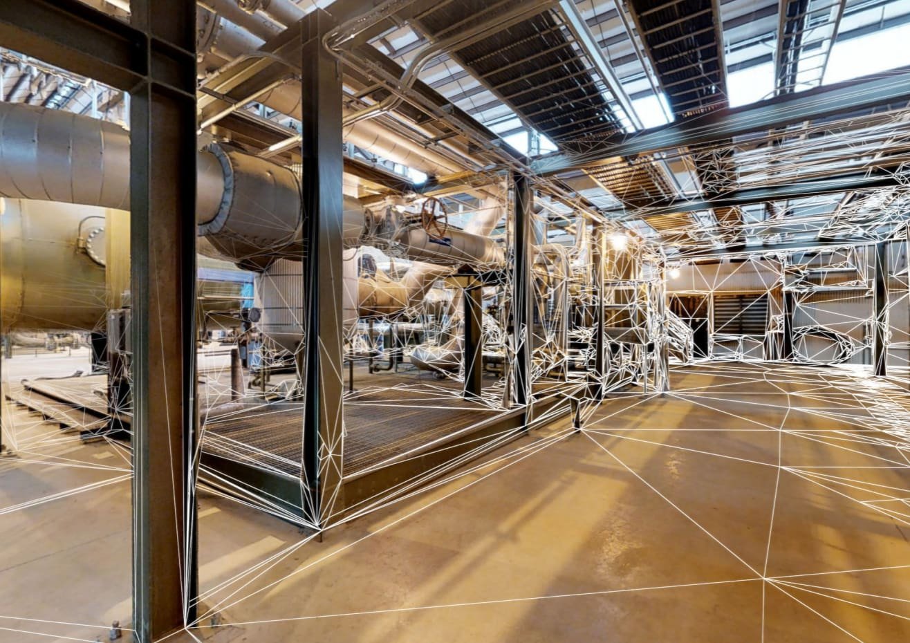 Industrial facility with large metal pipes and machinery, overlaid with white geometric lines creating a mesh pattern.